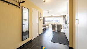 Een hotelgang met een spiegelkast, een droogrek en een stadszicht door grote ramen.