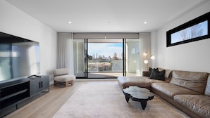 Una sala de estar moderna con un televisor de pantalla plana grande, un sofá de cuero, una mesa de centro y vistas de la ciudad a través de amplios ventanales.