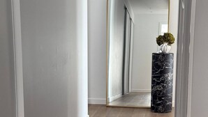 Un pasillo con un espejo grande, una columna de mármol y una planta pequeña en maceta.