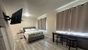 Een slaapkamer met een bed, nachtkastje, lamp en een raam met gordijnen.