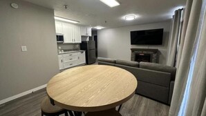 Een moderne woonkamer met een ronde houten tafel, een grijze bank en een flatscreen televisie aan de muur.