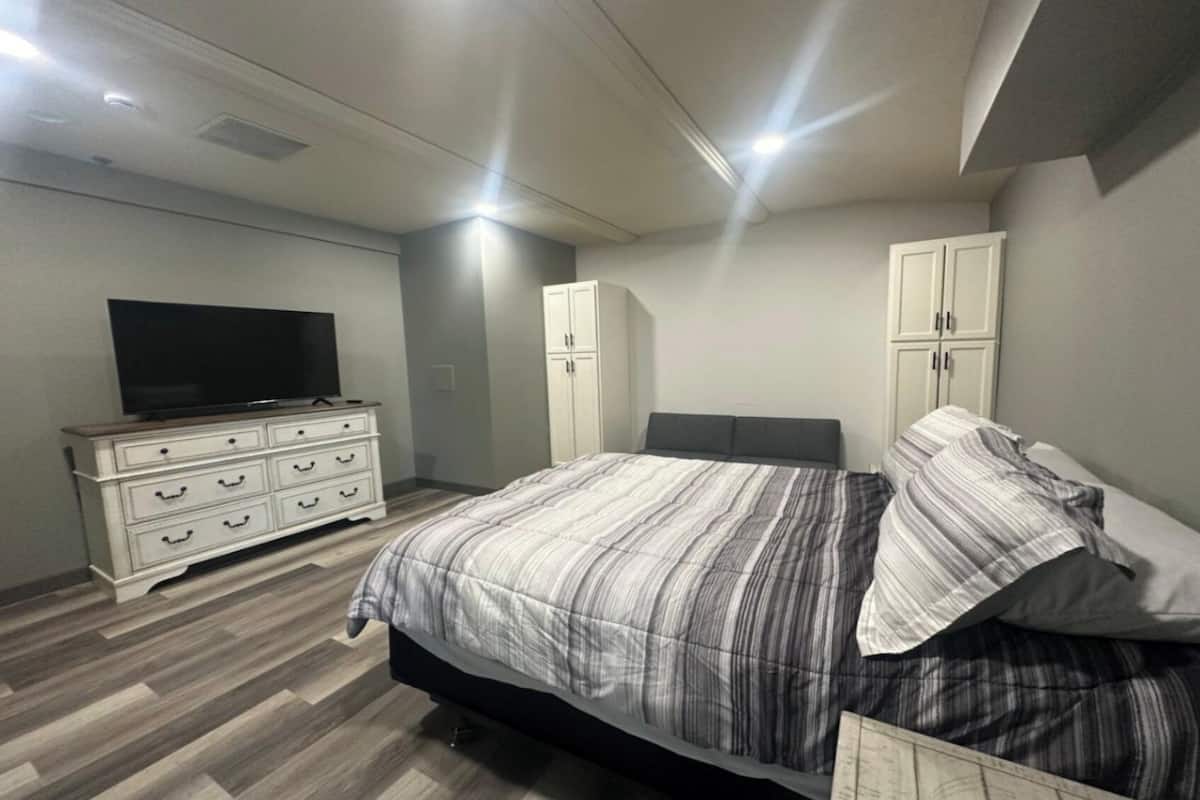 Een slaapkamer met een bed, dressoir, televisie en kasten.