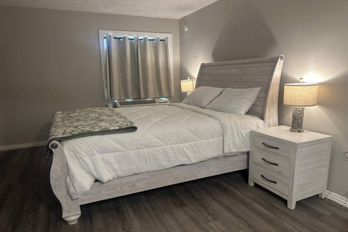 Een slaapkamer met een bed, nachtkastjes, een lamp en een raam met gordijnen.