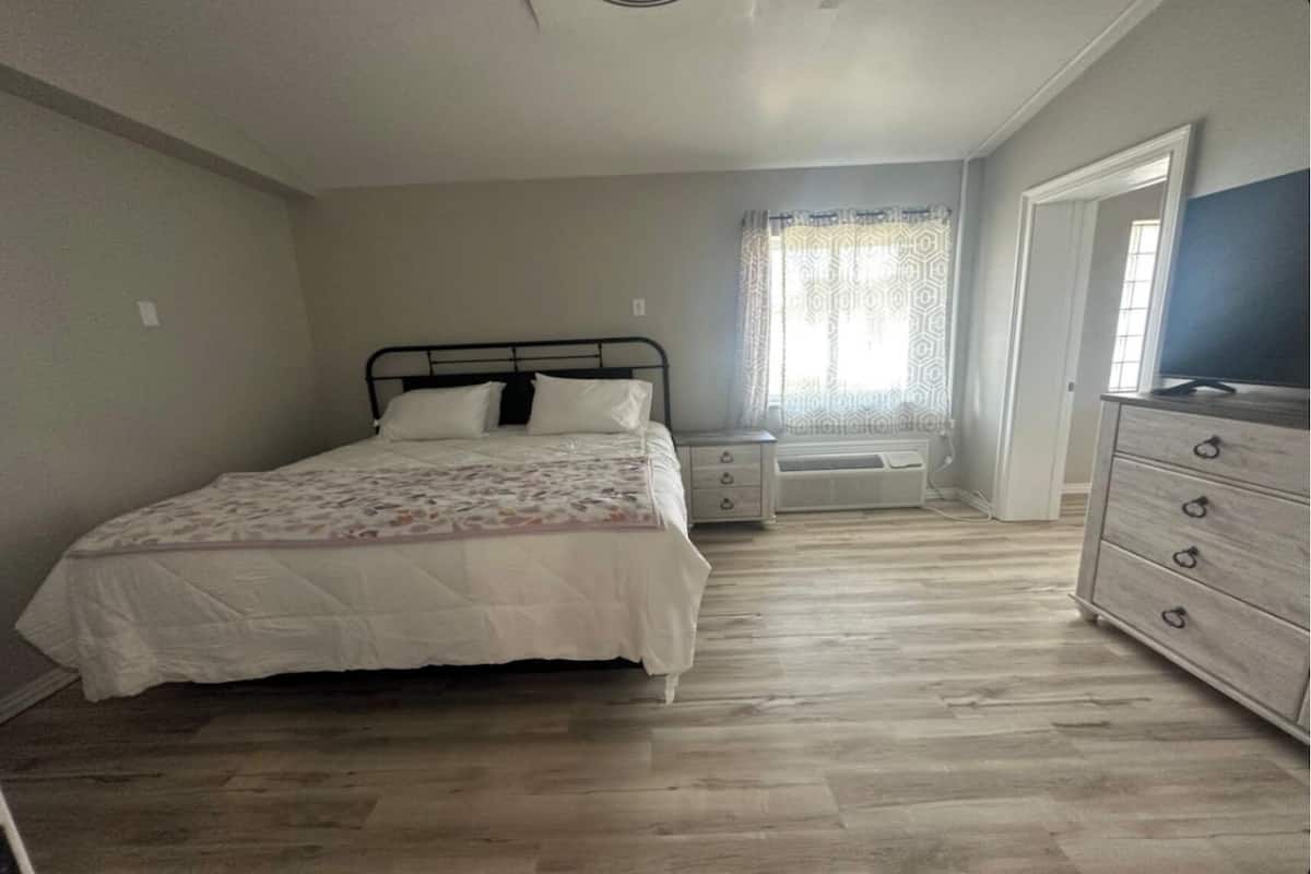 Een slaapkamer met een bed, een dressoir, een verwarming en een raam met gordijnen.