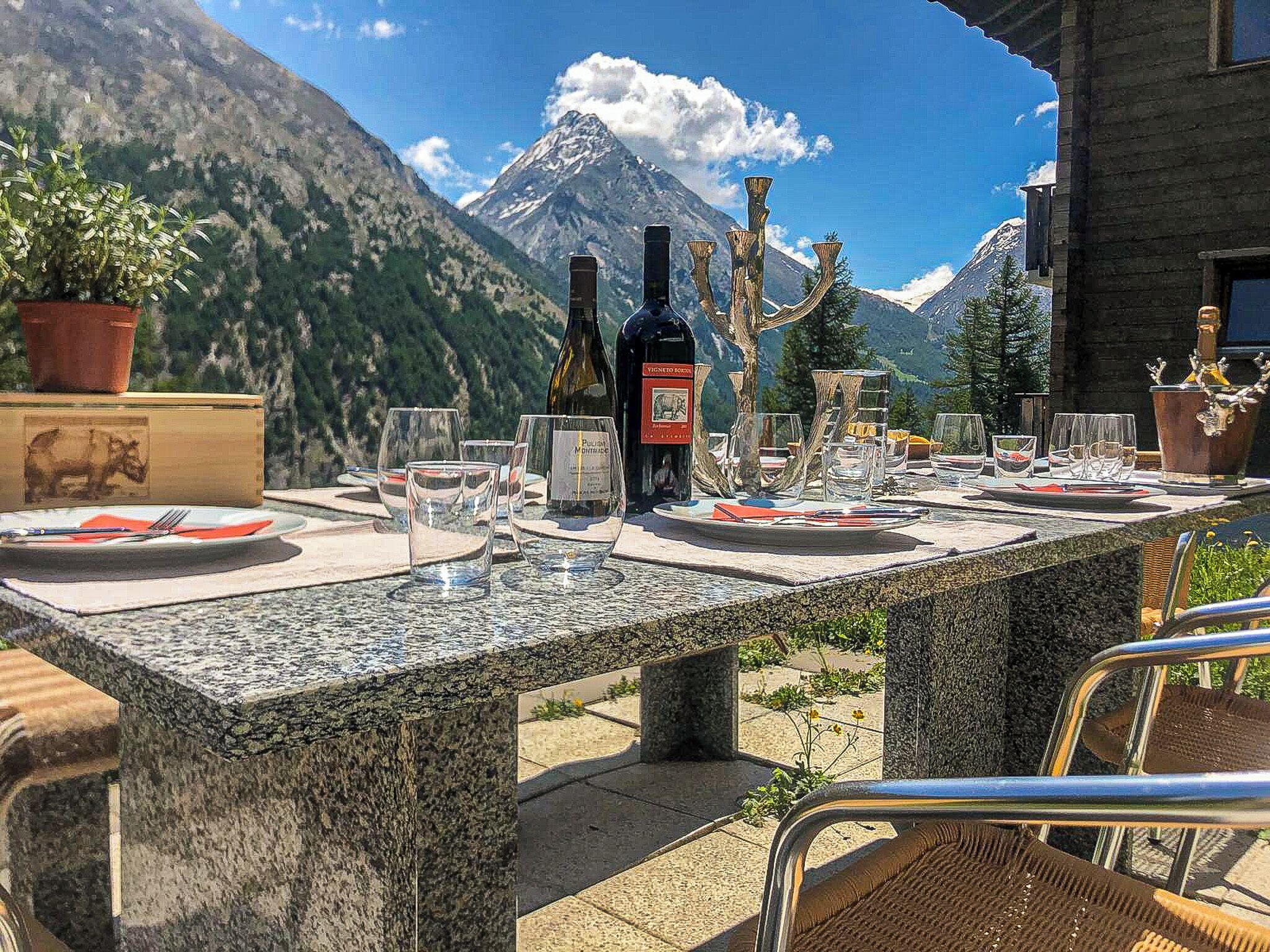 Une table dressée en plein air, avec une vue sur les montagnes, une bouteille de vin et un chandelier.