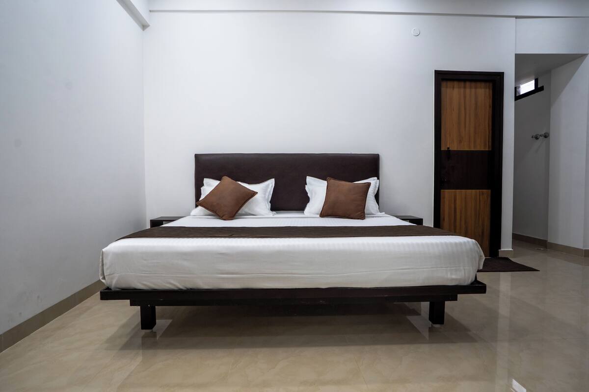 Un dormitorio moderno con una cama grande, ropa de cama blanca y almohadas marrones.