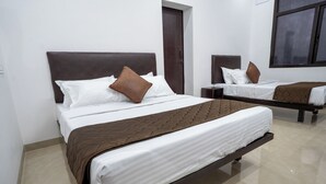 Une chambre d’hôtel avec deux lits, chacun doté d’une tête de lit marron, de draps blancs et d’un plaid marron.