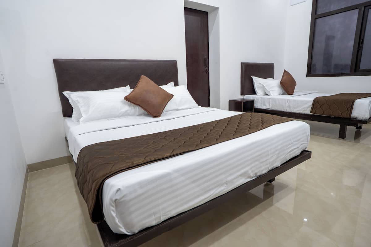 Habitación de hotel con dos camas, cada una con cabecero marrón, ropa de cama blanca y una manta marrón.