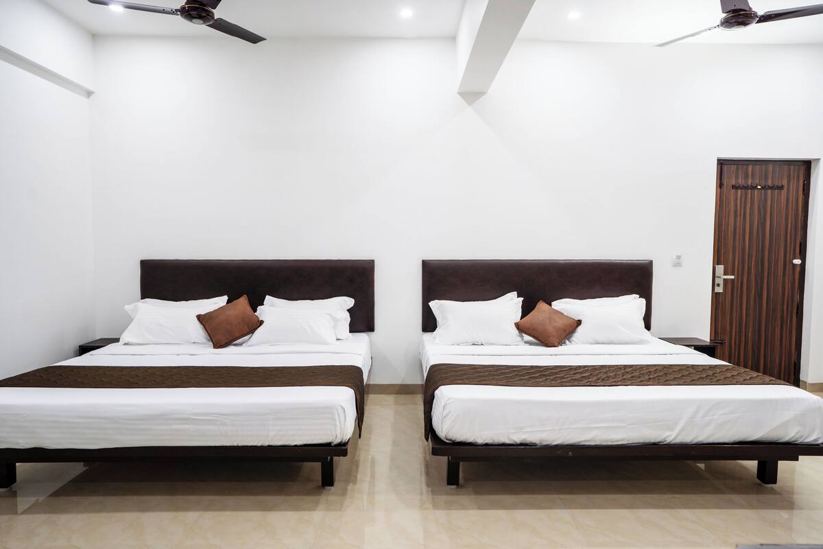 Habitación de hotel con dos camas, ropa de cama blanca, cabeceros marrones y una puerta de madera.