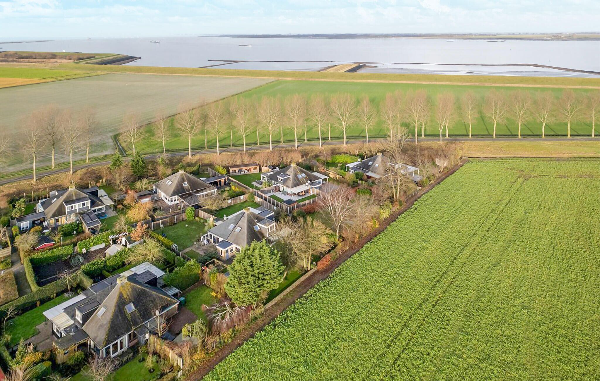 An aerial view of a residential area with houses, a large green field, and a body of water in the background.