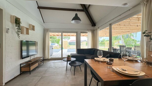 Una sala de estar moderna con televisor, sofá, mesa de comedor y ventanas amplias.