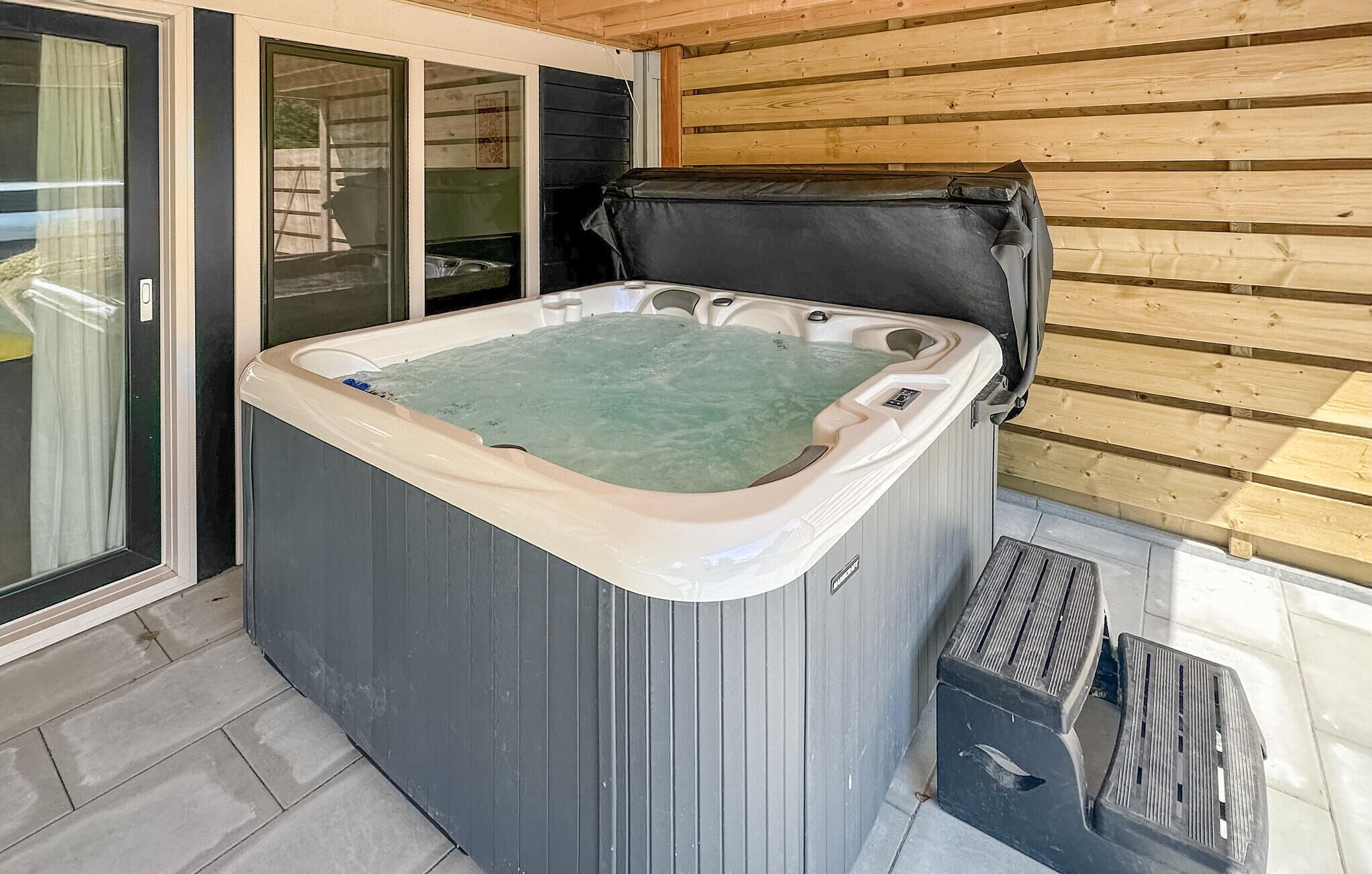 A hot tub with a wooden exterior, a glass door, and a wooden deck.