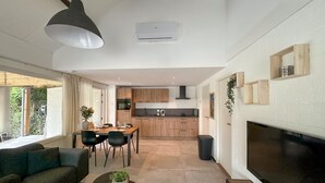 Una cocina moderna con armarios de madera, un comedor con mesa y sillas, y un televisor grande montado en la pared.