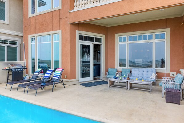 A poolside area with lounge chairs, a barbecue grill, and a seating area with a table and chairs.