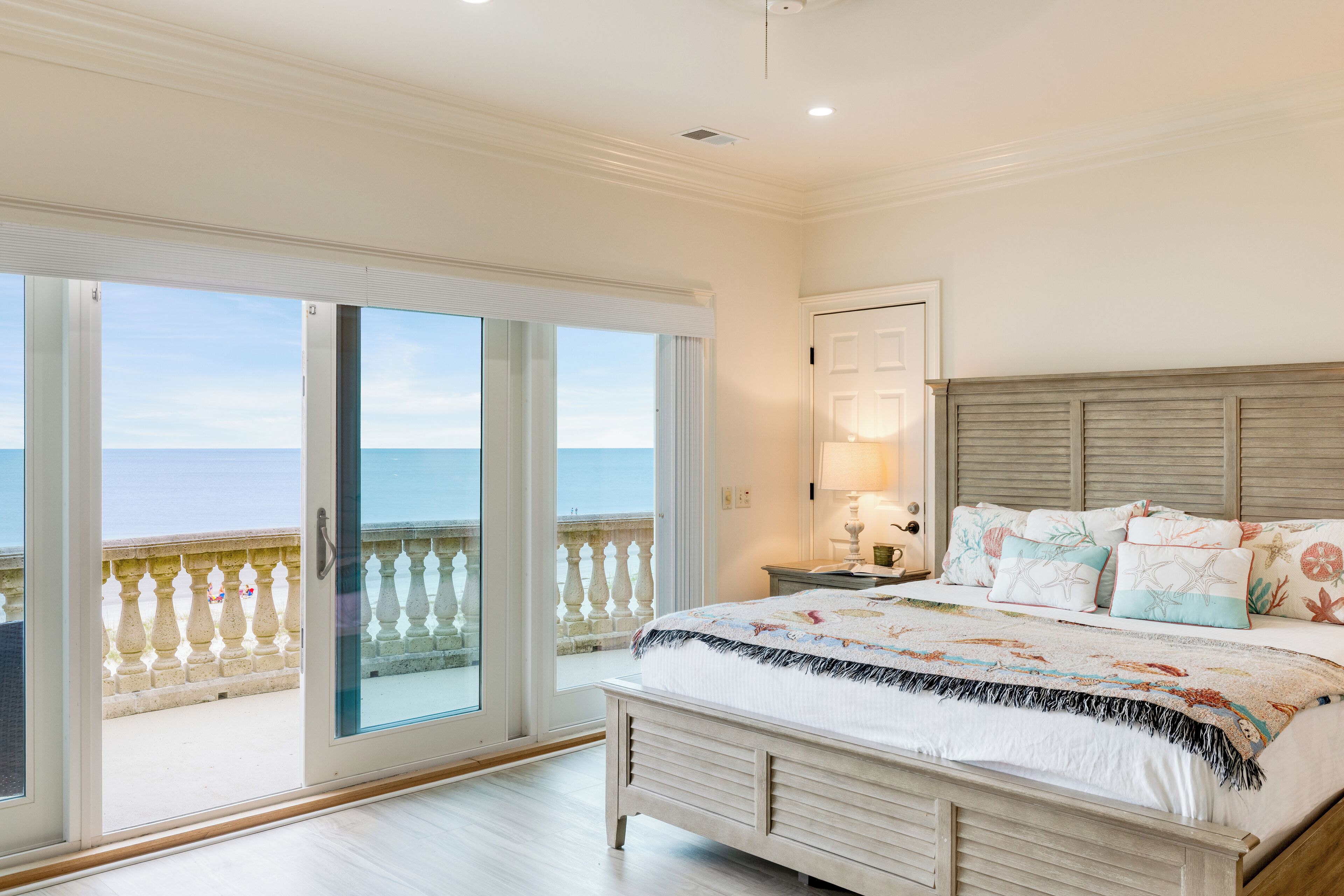 Une chambre avec un grand lit, une table de chevet, une lampe et une vue sur la mer, visible à travers une porte-fenêtre coulissante.