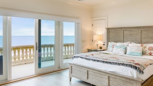 Une chambre avec un grand lit, une table de chevet, une lampe et une vue sur la mer, visible à travers une porte-fenêtre coulissante.