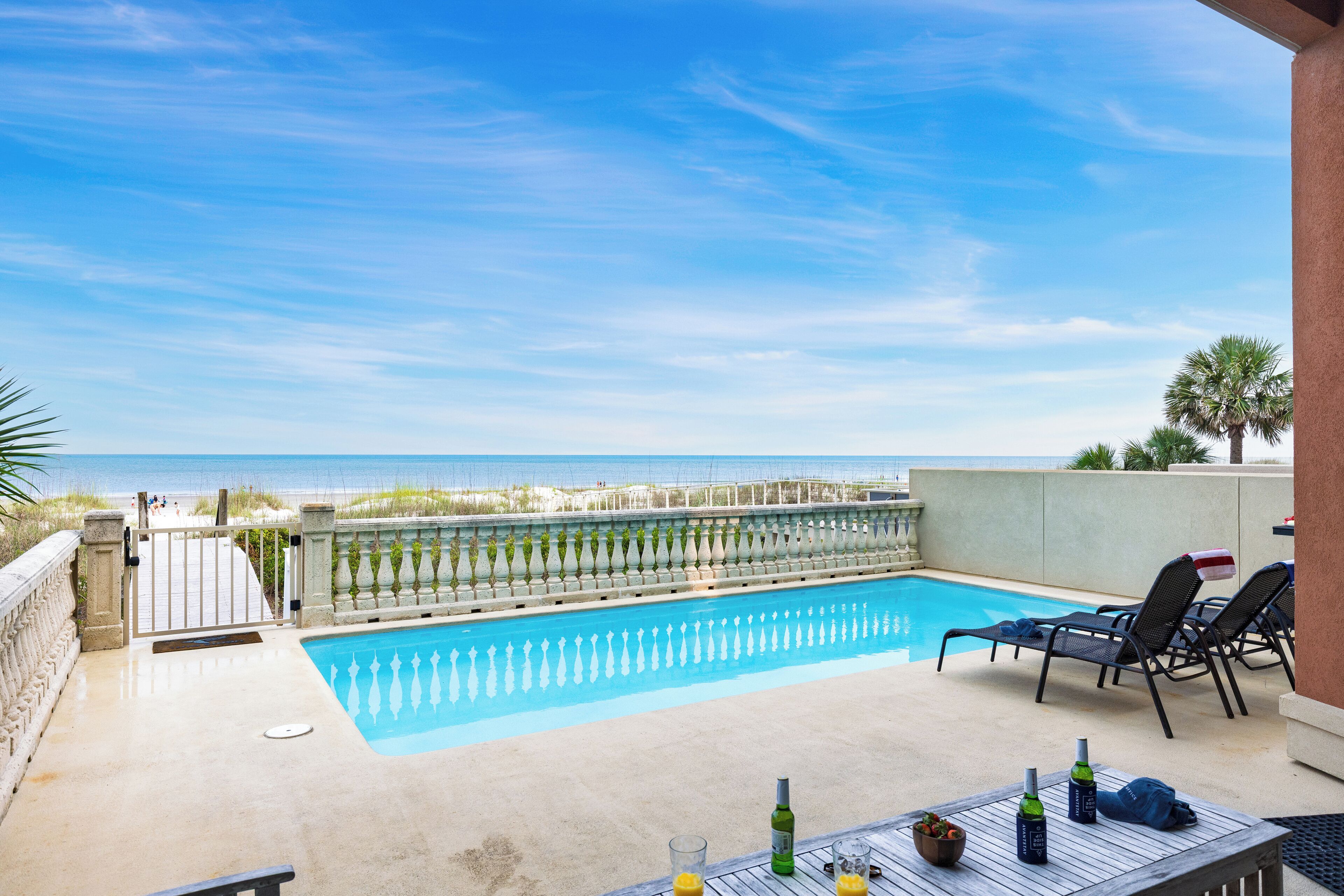 Ein Pool mit Blick auf den Strand, Liegestühle und ein Tisch mit Flaschen.