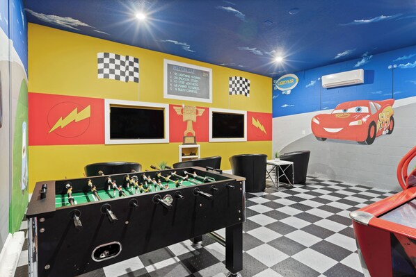 Una habitación con una mesa de fútbol de mesa, piso a cuadros y un mural con temática de carreras.