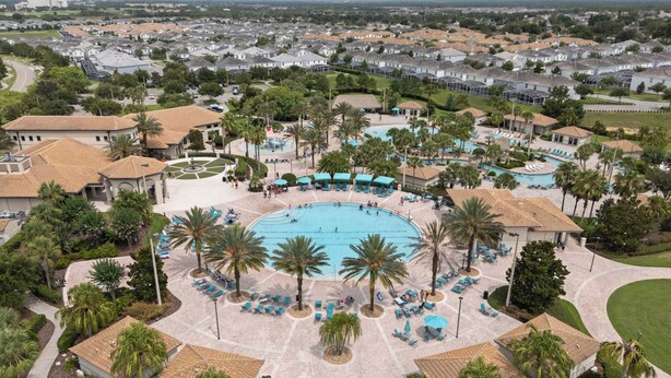 An aerial view of a resort with a central swimming pool surrounded by palm trees and lounge areas.