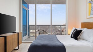 A modern hotel room with a large bed, a flat-screen TV, and a balcony with city views.