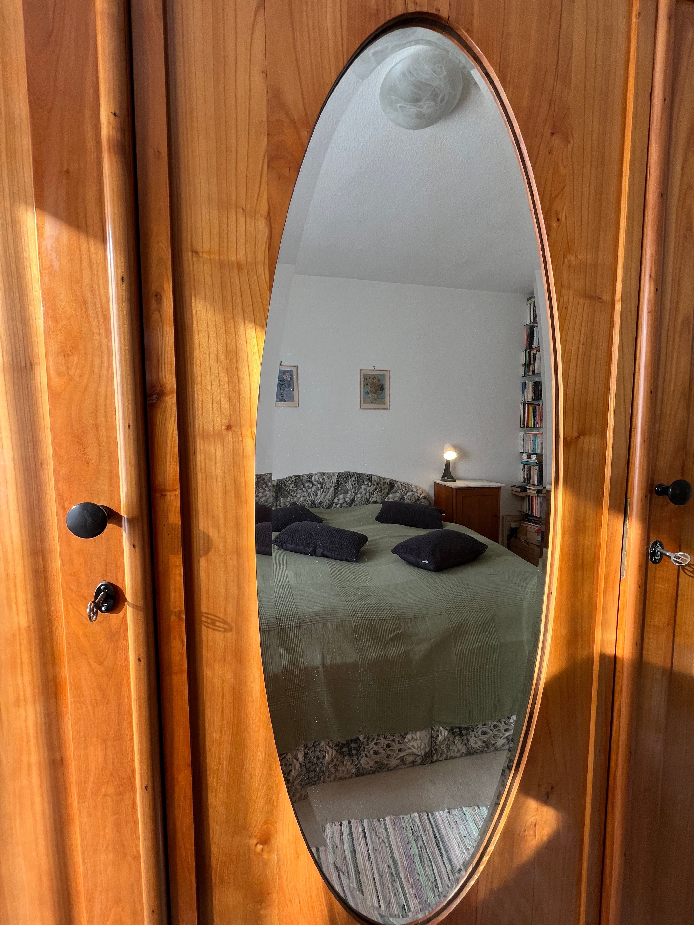 A bedroom with a bed, pillows, a nightstand, and a mirror reflecting the room.
