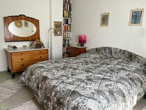 A bedroom with a large bed, a dresser, a mirror, a bookshelf, and a lamp.