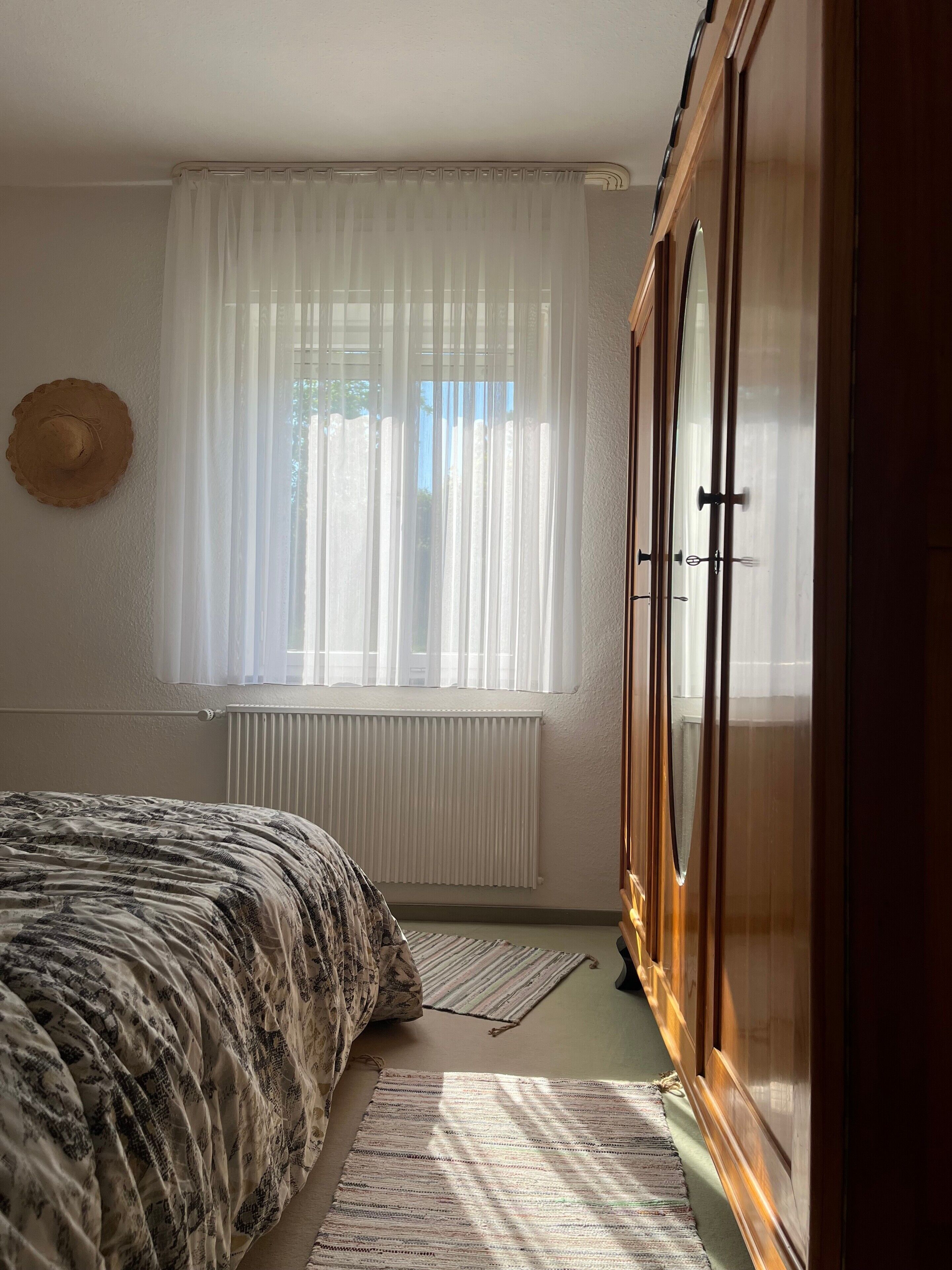 Una camera da letto con un letto, un termosifone, una finestra con tende leggere e un armadio in legno.