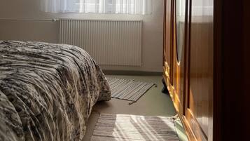 Una camera da letto con un letto, un termosifone, una finestra con tende leggere e un armadio in legno.