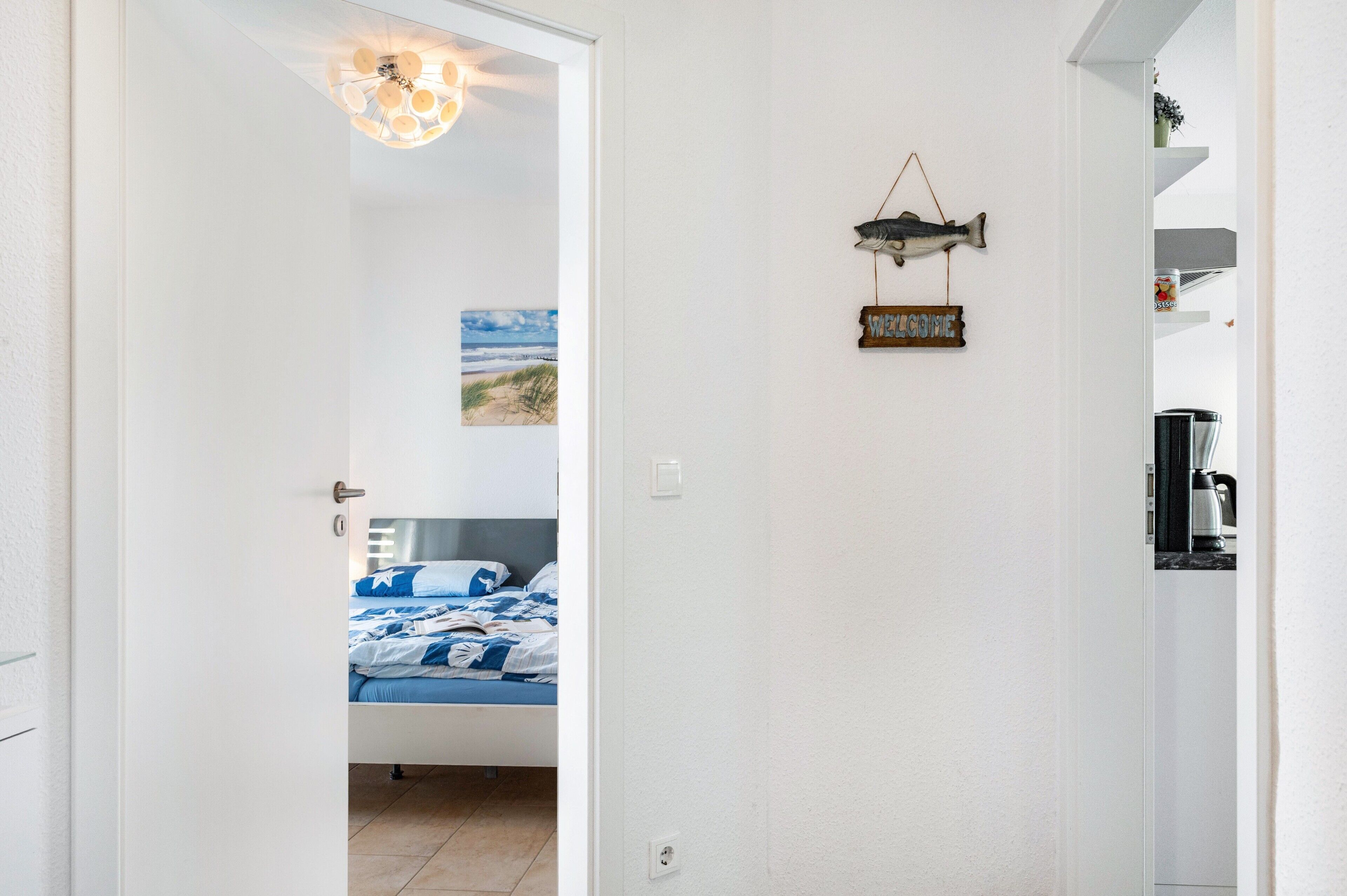 A bedroom with a bed, a wall-mounted light fixture, a welcome sign, and a painting.