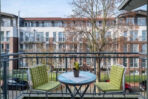A balcony with two chairs and a table, a potted plant, and a view of a multi-story building with balconies.