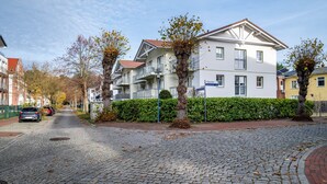 A residential street with cobblestone pavement, a white two-story building with balconies, and a hedge in the foreground. - Apartment 'Direkt Am' with Balcony and Wi-Fi (Graal-Müritz)