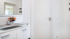 A white bathroom with a glass-topped vanity, a mirror, a door, and a small window. - Apartment 'Direkt Am' with Balcony and Wi-Fi (Graal-Müritz)