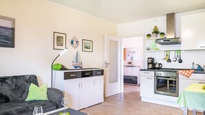 A compact living space with a sofa, dining table, kitchenette, and a door leading to another room. - Apartment 'Direkt Am' with Balcony and Wi-Fi (Graal-Müritz)