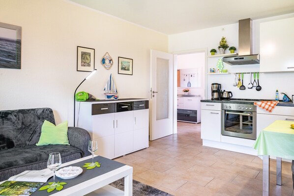 A compact living space with a sofa, dining table, kitchenette, and a door leading to another room.