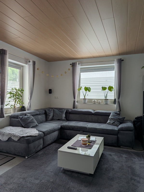 Una sala de estar moderna con un sofá modular, una mesa de centro y un ventanal con cortinas.