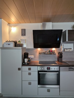Una cocina moderna con microondas integrado, horno y estufa. Hay armarios, una cafetera y un estante para especias.