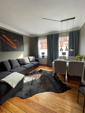 A modern living room with a sofa, dining table, chairs, a rug, and a large abstract painting.