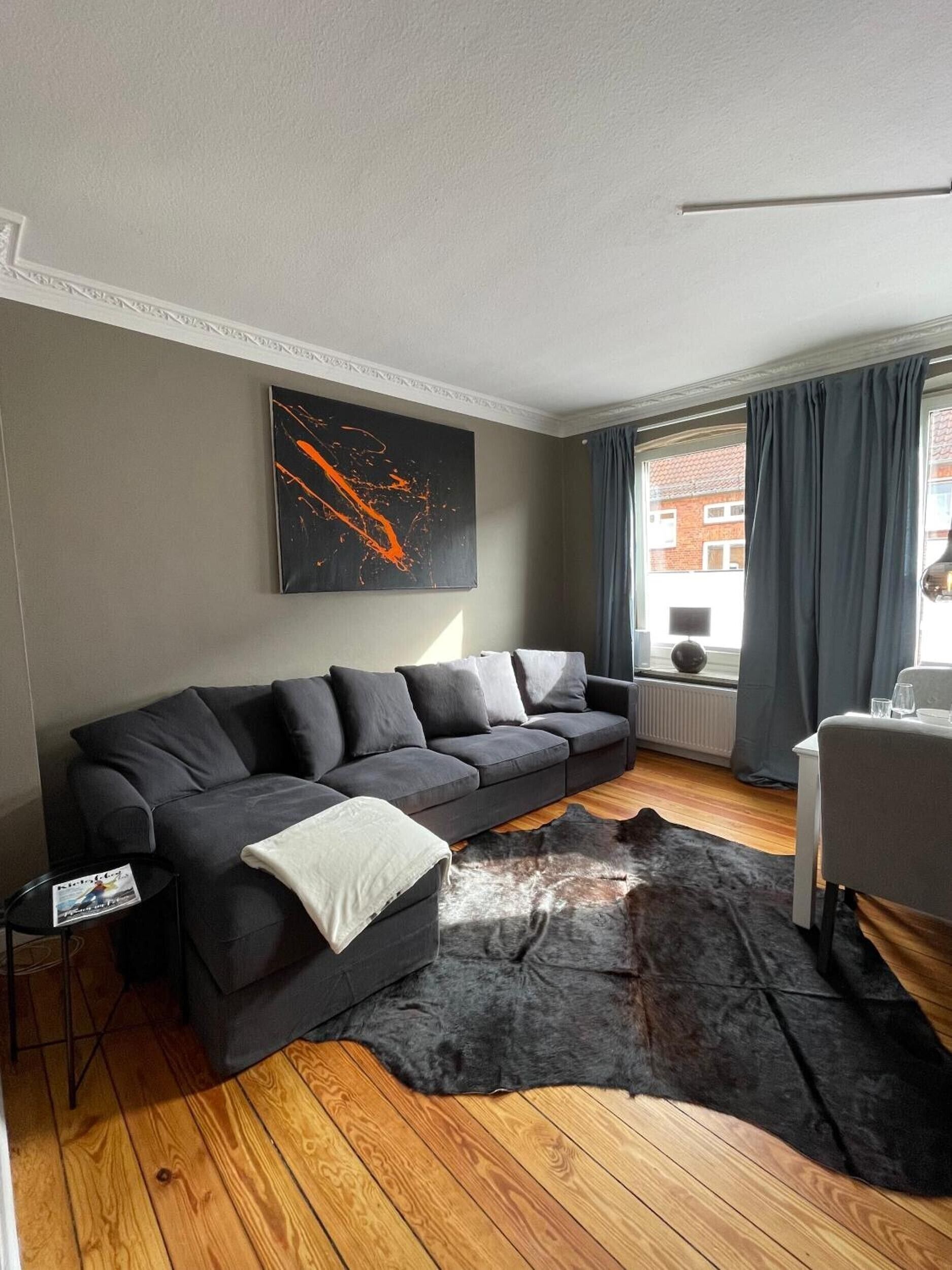 A modern living room with a sectional sofa, a large abstract painting, a fur rug, and a dining area with a table and chairs.