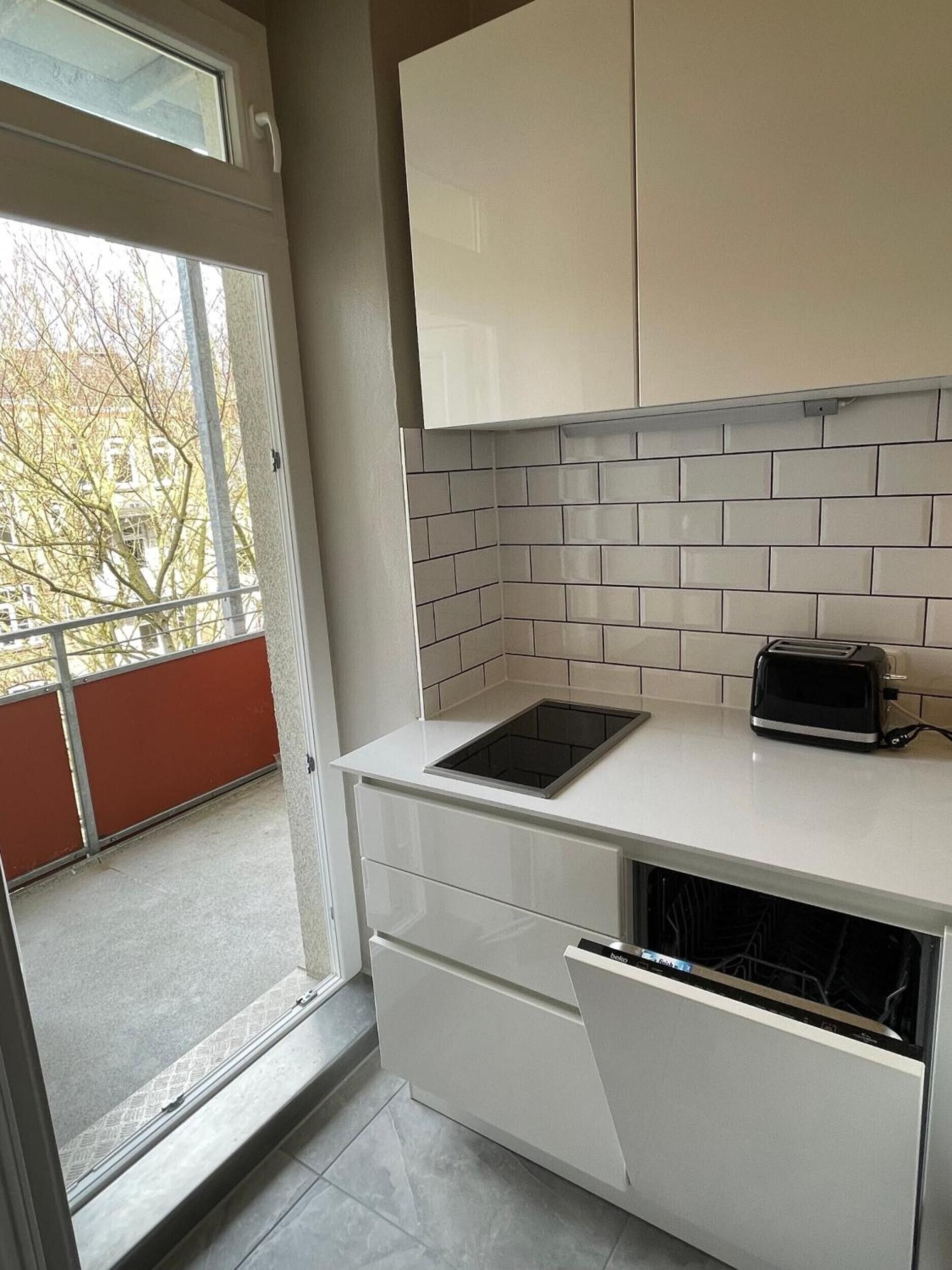 A modern kitchen with white cabinets, a tiled backsplash, a built-in toaster, and a sliding door leading to a balcony.