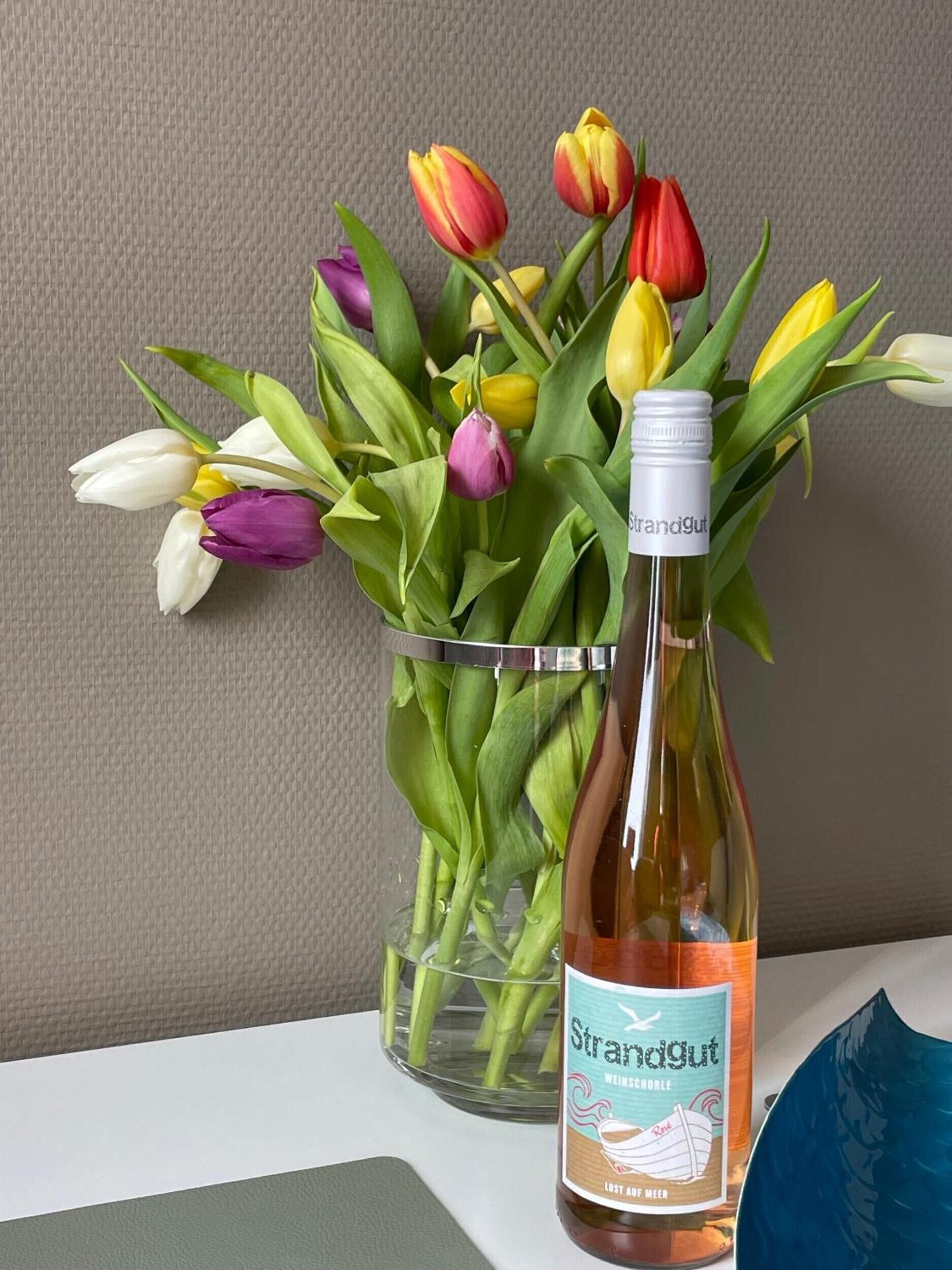 Una botella de Strandgut Weissborl sobre una mesa con un ramo de tulipanes.