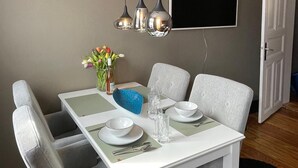 Un comedor con una mesa blanca, sillas grises, un tazón azul y un florero con flores.