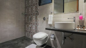 A modern bathroom with a white toilet, a sink with a mirror above it, and a shower area with patterned tiles.