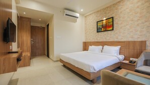 A hotel room with a bed, a desk, a chair, a TV, and an air conditioning unit.
