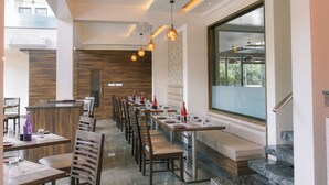 A modern restaurant with a long dining area, wooden accents, and a large window offering a view.