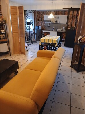 Un salon avec un canapé, une table à manger et des chaises, un coin cuisine et un escalier.