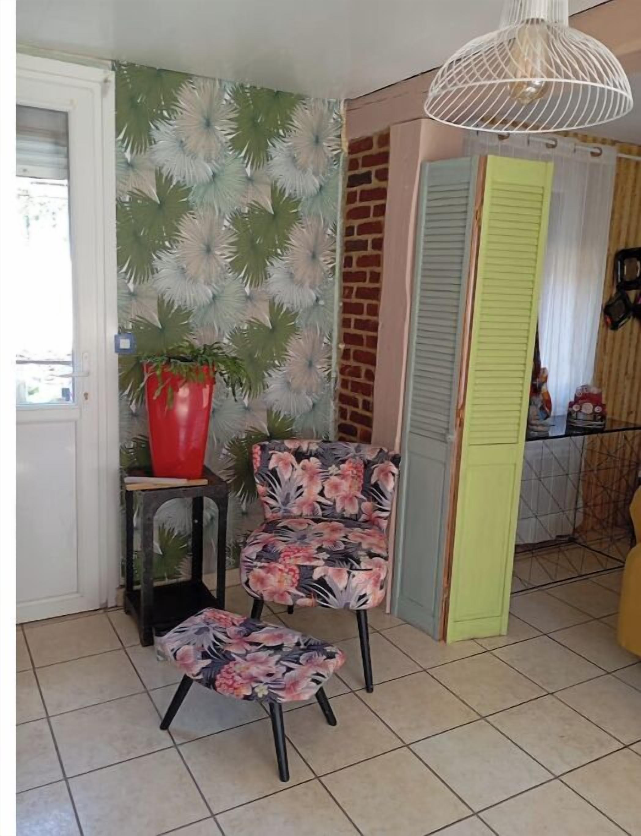 Une cuisine avec un sol carrelé, une plante en pot rouge, une chaise à motifs floraux et un luminaire suspendu.