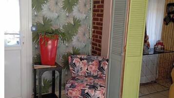 Une cuisine avec un sol carrelé, une plante en pot rouge, une chaise à motifs floraux et un luminaire suspendu.