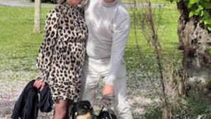 Une personne portant une robe à motifs léopard et une tenue blanche, debout à côté d’un chien.