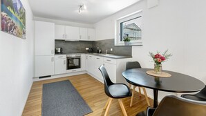 A modern kitchen with white cabinets, a dining table with chairs, a rug, and a window with a view of a building. - Apartment 'Seeglück' with Mountain View, Private Terrace and Wi-Fi (Bodman-Ludwigshafen)
