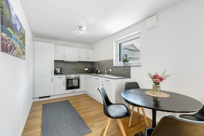 Una cocina moderna con armarios blancos, una mesa de comedor con sillas, una alfombra y una ventana con vistas a un edificio.